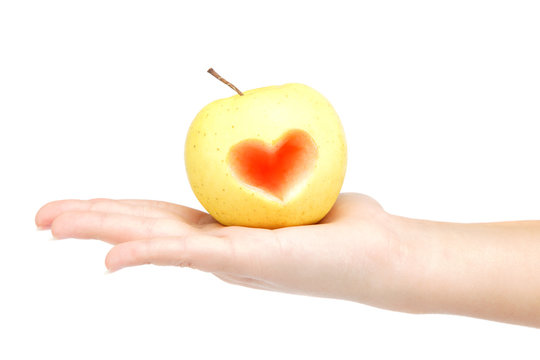 Woman's hand holding an apple with a carved image of the heart o