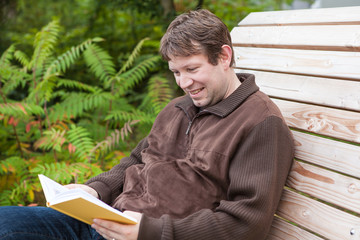 Young man reading book on bench in summer forest