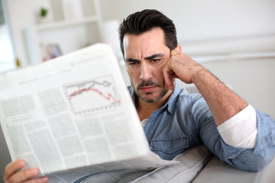 Man at home reading bad news on newspaper