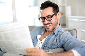 Cheerful guy reading newspaper in sofa