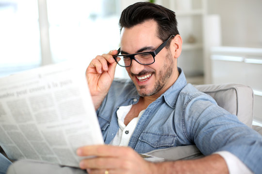 Cheerful guy reading newspaper in sofa