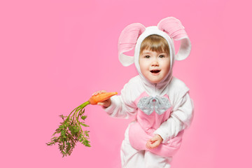 Child in bunny hare costume holding carrots. Pink background