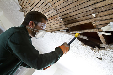 man removing plaster lathe from ceiling with a crowbar.