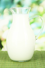 Pitcher of milk on table on bright background