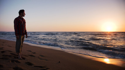 Man standing on the beach and looking into sunset
