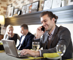 Businessman sitting at table in cafe using laptop computer, talk