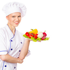 Joyful woman cook in chefs cap with pure vegetables on plate