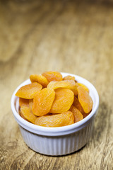 A handful of dried apricots in a ceramic white bowl on the woode