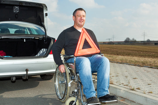 Man in a wheelchair and warning triangle next to his car