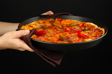 hands holding pepperoni pizza in pan isolated on black