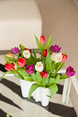 Colorful tulips in white vase on table in living room.
