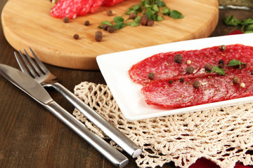 Tasty salami on plate and board on wooden table close-up