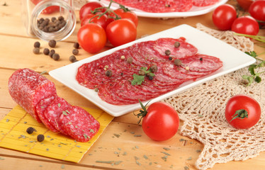 Tasty salami on plates on wooden table close-up