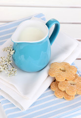 Blue jug with milk and cookies on wooden picnic table close-up