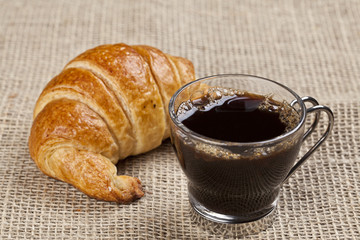 A cup of coffee with a croissant