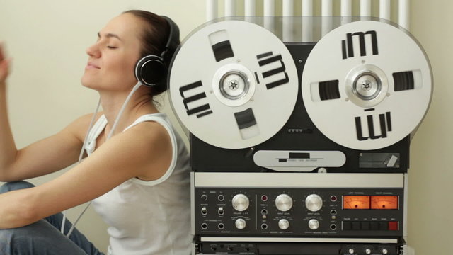 Girl in headphones listening to music from retro tape recorder