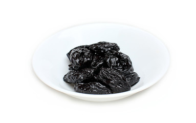 Dried prunes in a white plate on a white background