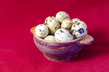 Quail eggs in clay bowl, red background