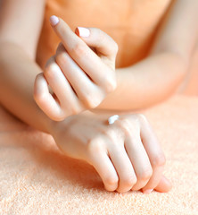 Fototapeta premium Young woman applies cream on her hands after bath. Focus on hand