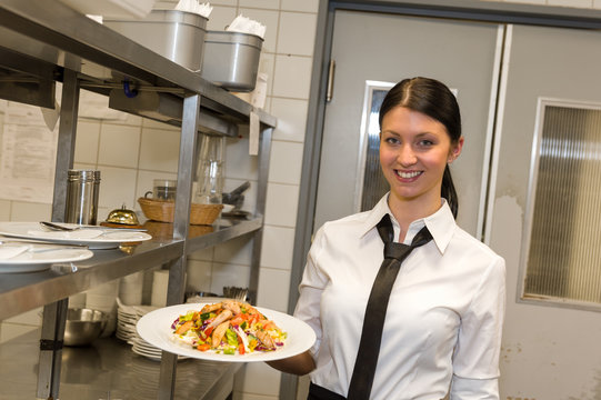 Smiling waitress serving salad on plate