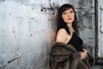 Fototapeta premium Sensual dark-haired woman in fur coat standing by the wall