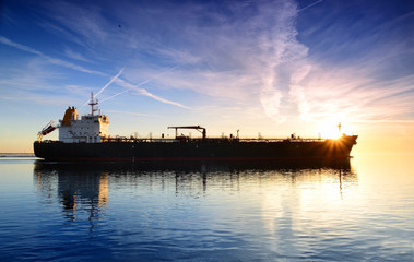 Cargo ship sailing away against colorful sunset
