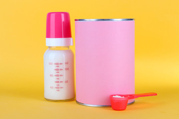 Powdered milk with baby bottle of milk on yellow background
