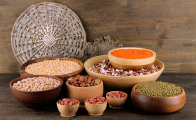 Different kinds of beans in bowls on wooden background