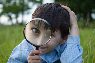 Boy with magnifying glass lying on the grass