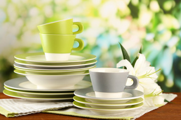 Empty plates and cups on wooden table on green background