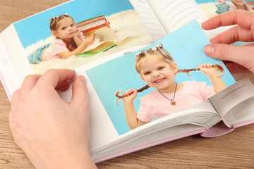 Photos in hands and photo album on wooden table