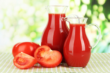 Tomato juice in pitchers on table on bright background
