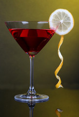 Red cocktail in martini glass on dark yellow background