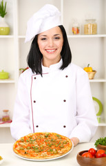 Beautiful girl chief-cooker with pizza on kitchen background