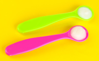 Color spoons for baby food on yellow background