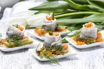 Pickled herring rolls with vegetables on wooden table