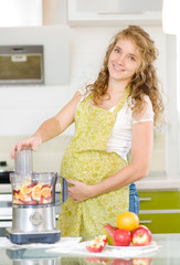 pregnant woman using a juicer, standing in the kitchen