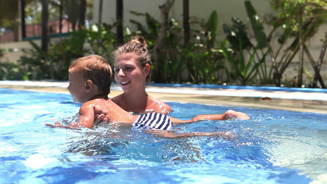 Happy mother teaching to swim daughter in swimming pool