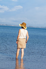 Woman with hat standing in the sea and looks into the distance