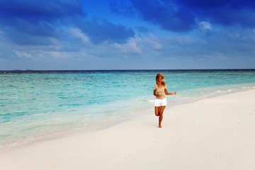 Fototapeta na wymiar The sporting woman runs on the seashore. Maldives