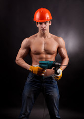 Muscular worker with an electric drill on a black background.