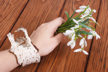 Obraz na płótnie Canvas Snowdrops in a female hand with a bracelet on a birch