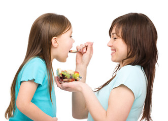 Mother is feeding her daughter with fruit salad