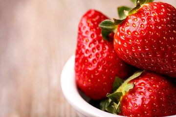 Strawberries in white plate on wooden table. 