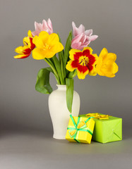 Beautiful tulips in bucket with gifts on grey background