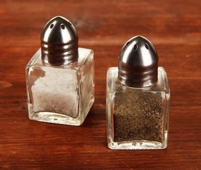 Containers for salt and pepper on wooden table close-up