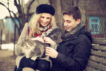 happy young couple with a cat on a bench near the house