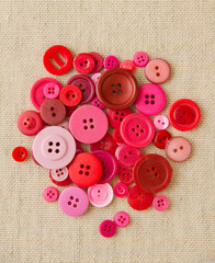 Pile of red and pink buttons on hessian
