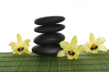 a pile of balanced zen stones with orchid on green mat