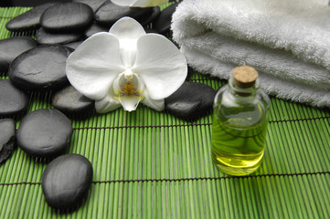 Orchid and stones with towel and massage oil on green mat